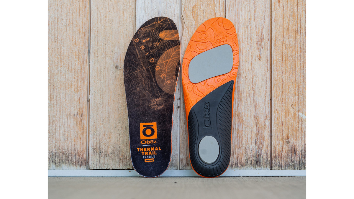 Oboz Thermal Trail insoles, one black and one orange, on a wooden background.