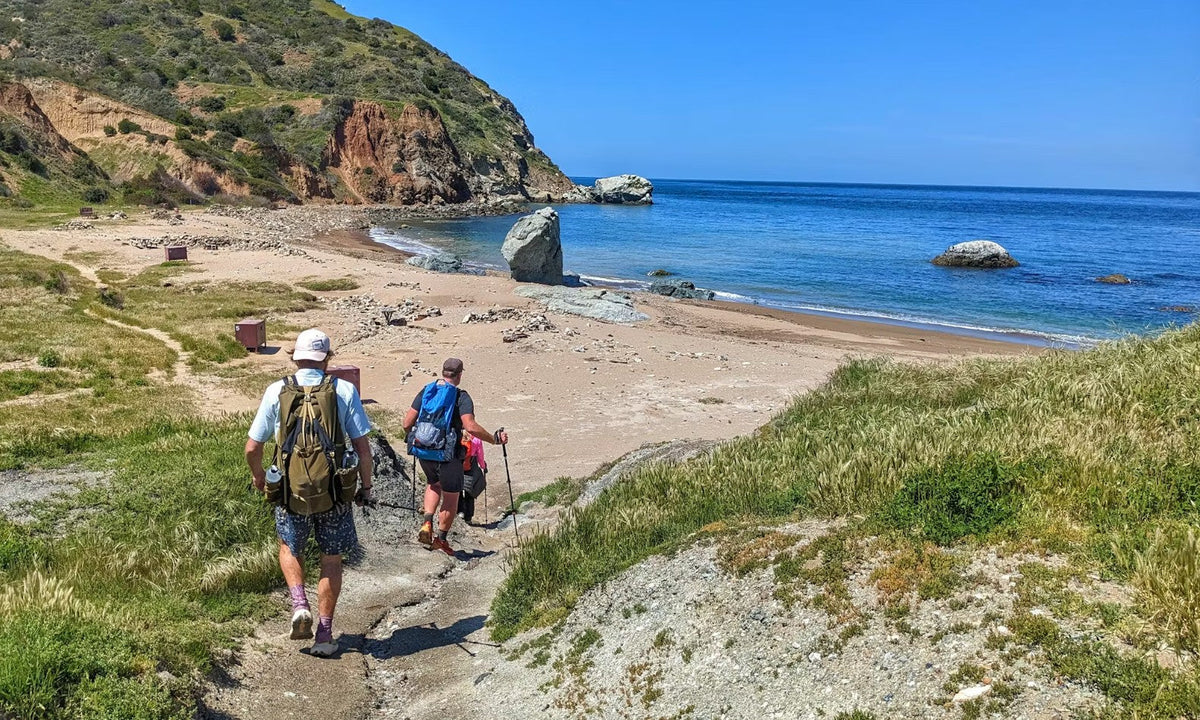 Hikers on the PCT in Oboz hiking shoes walk down to the beach.