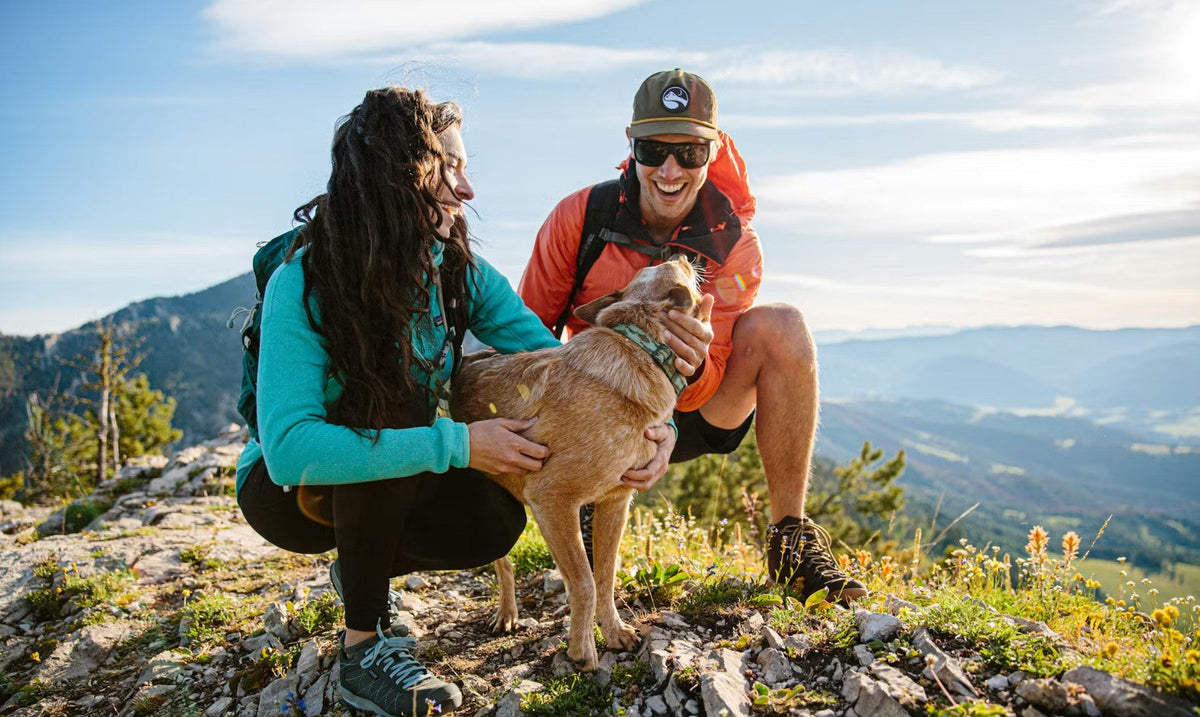 Two hikers wearing their Oboz hiking shoes stopped on a trail to pet a dog.
