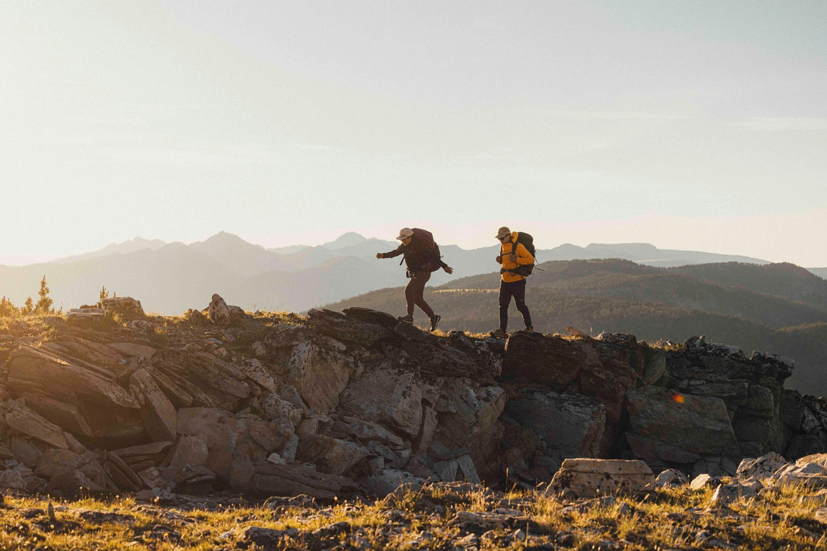 Two people hiking across a rocky ridge during golden hour.
