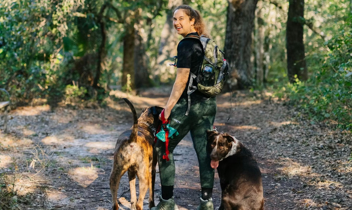 Woman hiking on a shady trail in Oboz Sypes Mid Leather B Dry hiking boots with two dogs