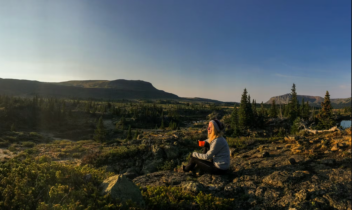 A girl sitting in the mountains sipping a cup of coffee