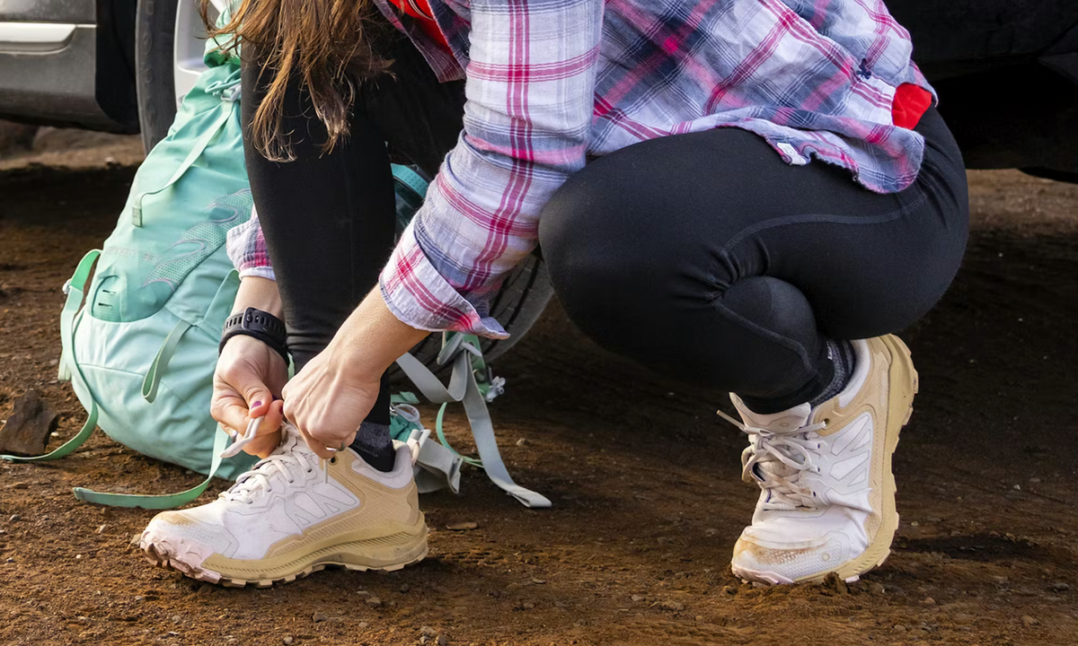 Woman tying her Katabatic Low Oboz hiking shoes before hiking on a trail.