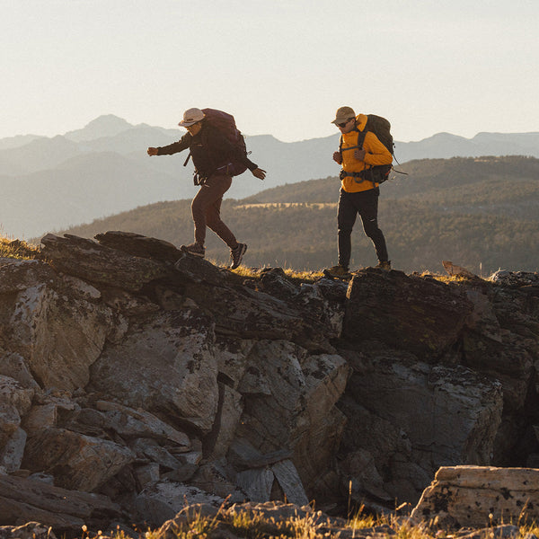 Person with a large backpacking backpack crosses a mountain stream in alpine terrain.