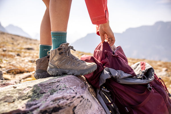 Woman loads gear into a pack while standing on a rock in Oboz Sawtooth hiking boots