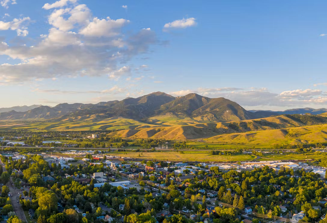 Aerial view of Bozeman, MT with greenery and mountains under a blue sky.