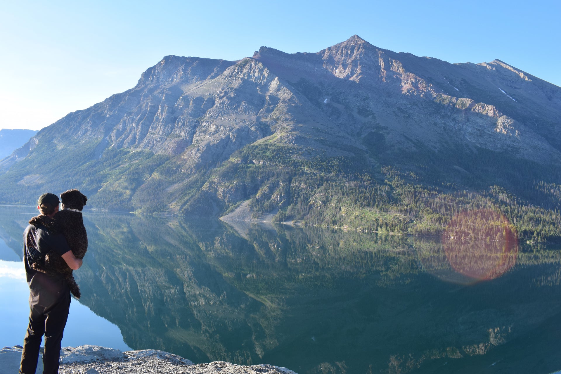 Person standing on a cliff overlooking a mountainous landscape with a lake.