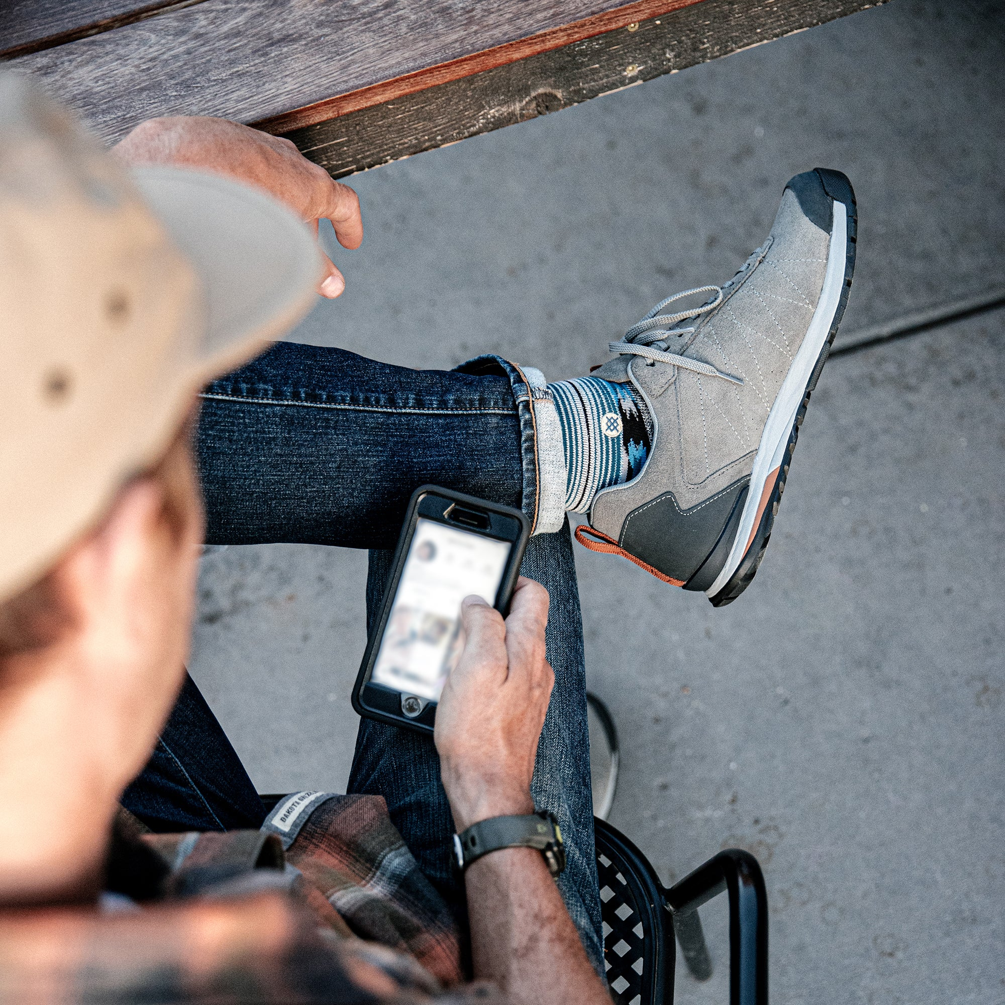 Person sitting on a chair using a smartphone while wearing the Oboz Bozeman Low Leather in Charcoal gray.