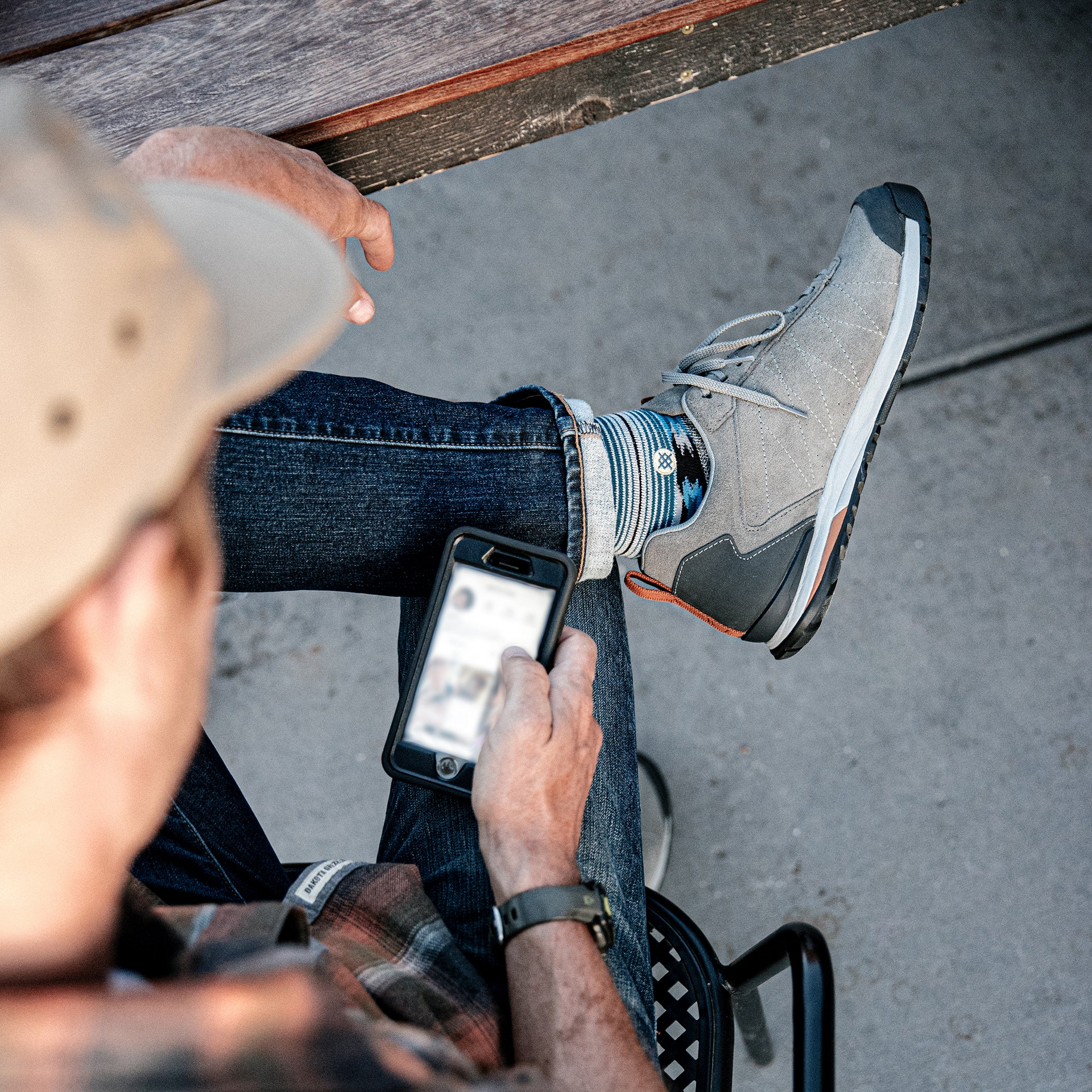 Person sitting on a chair using a smartphone while wearing the Oboz Bozeman Low Leather in Charcoal gray.