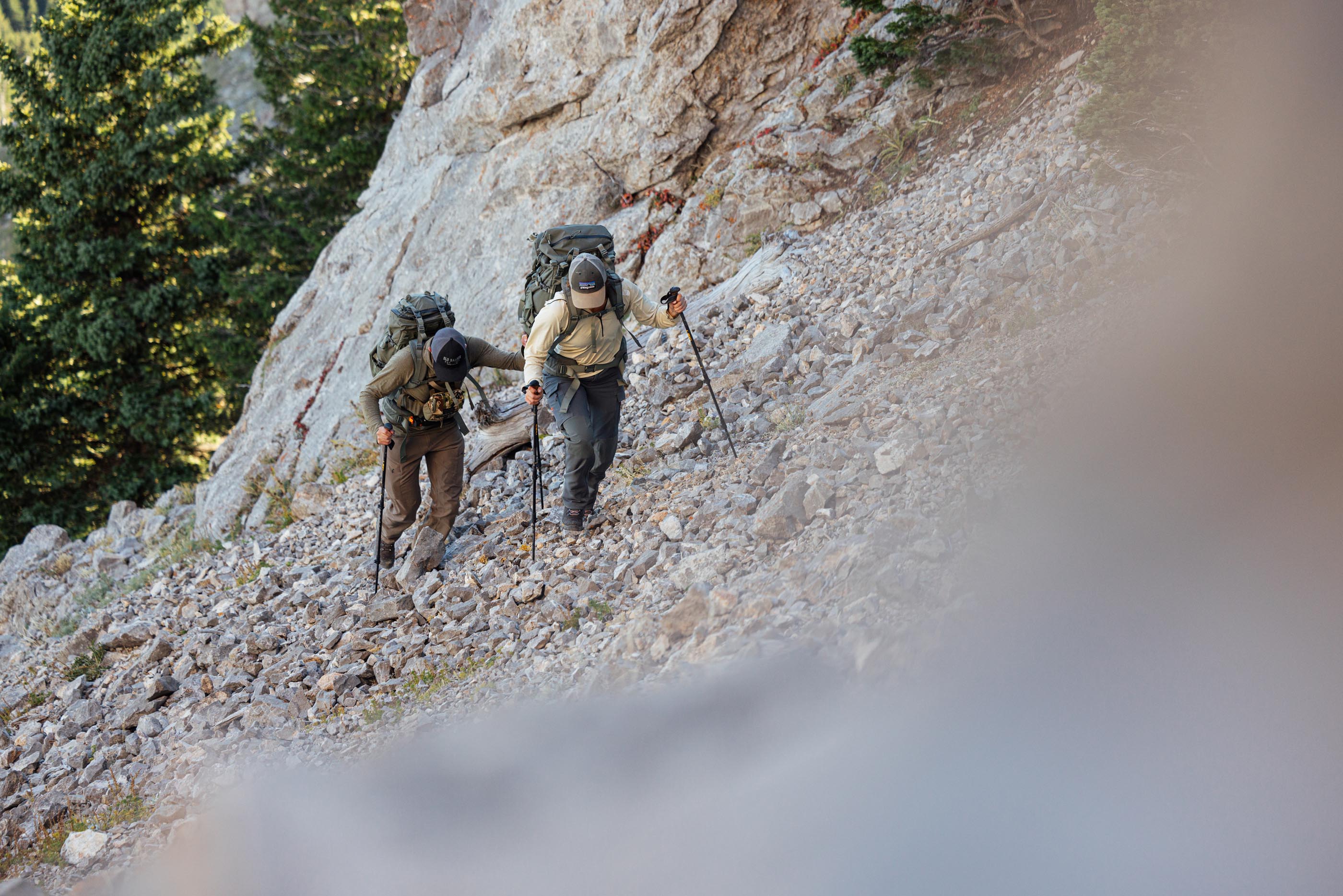Two hikers with backpacks climbing a rocky mountain trail.