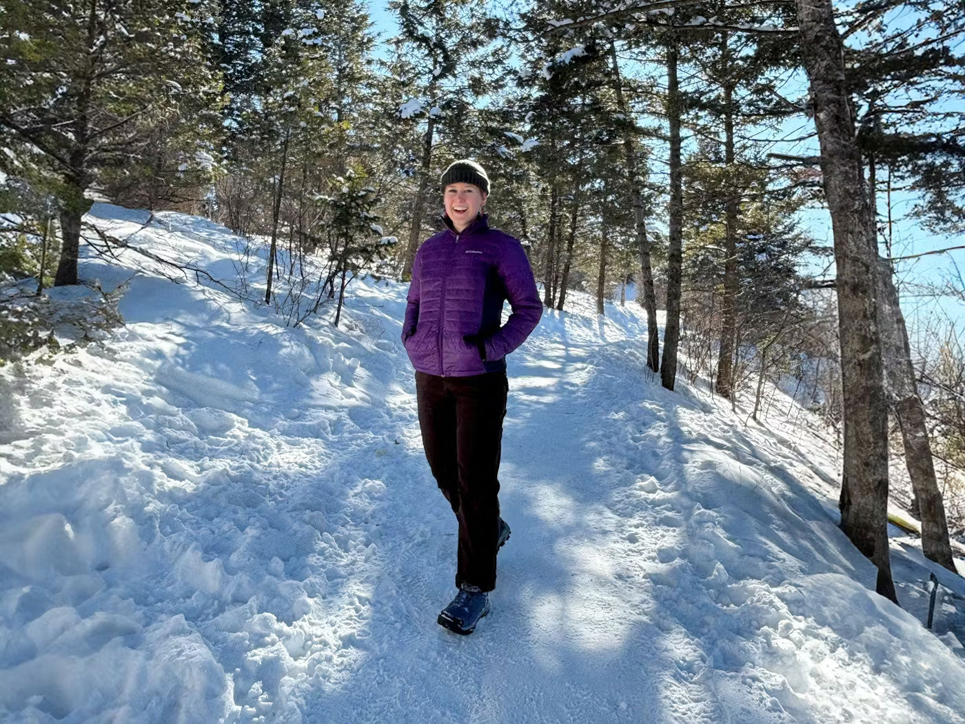 Person in a purple jacket walking on a snow-covered trail in a forest