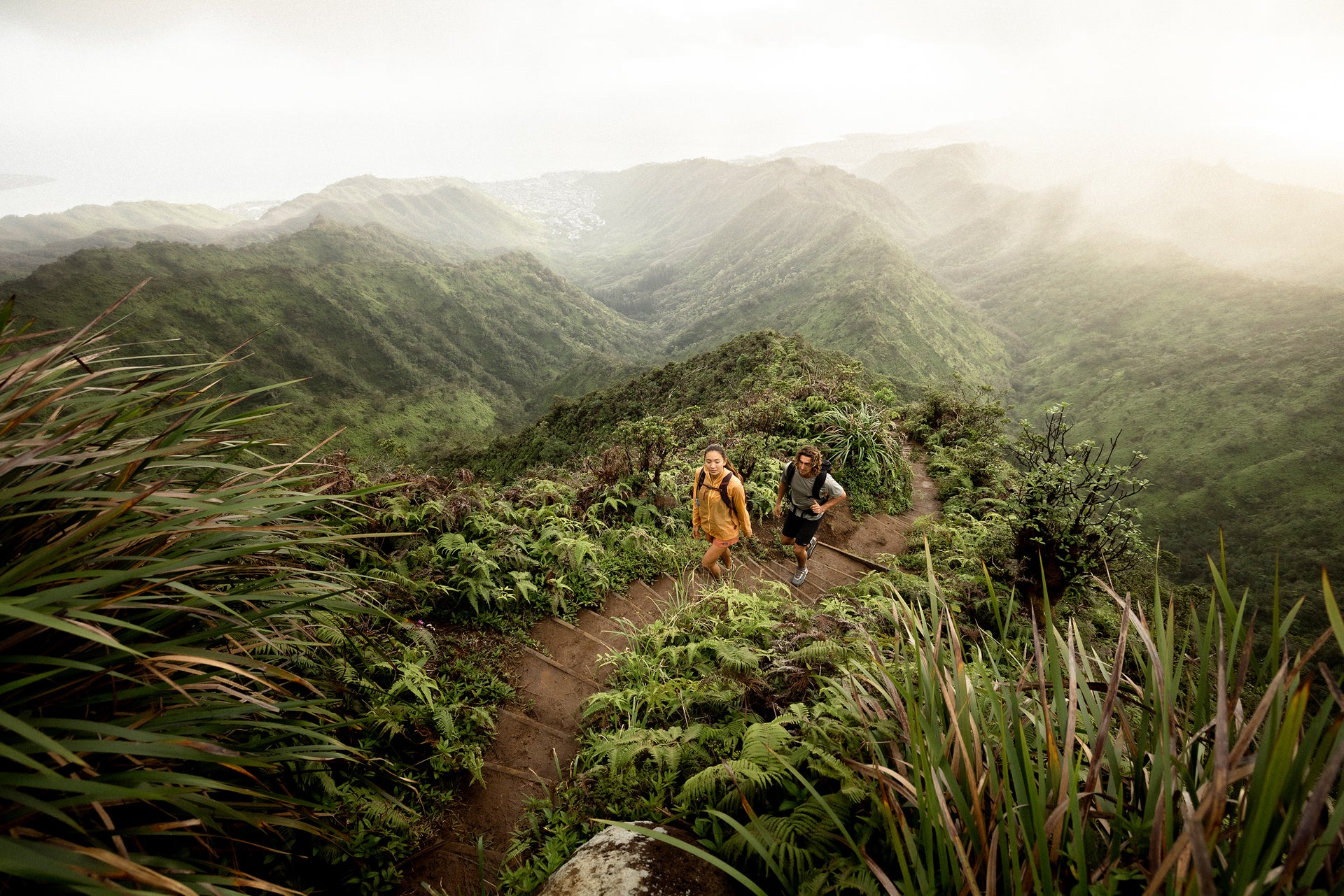 Two hikers on a trail surrounded by lush green mountains.