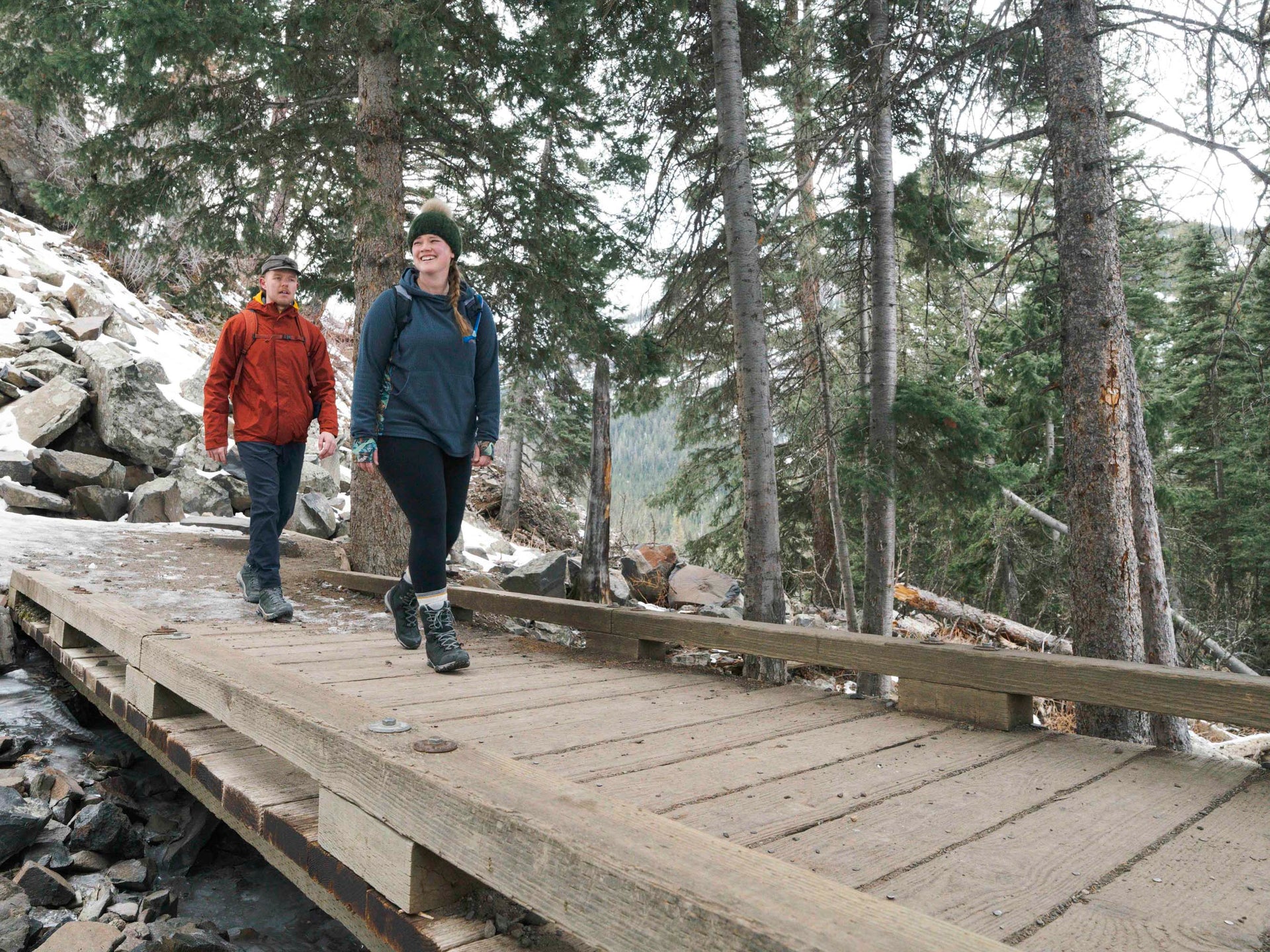 Two people hiking on a wooden bridge in a forested area.