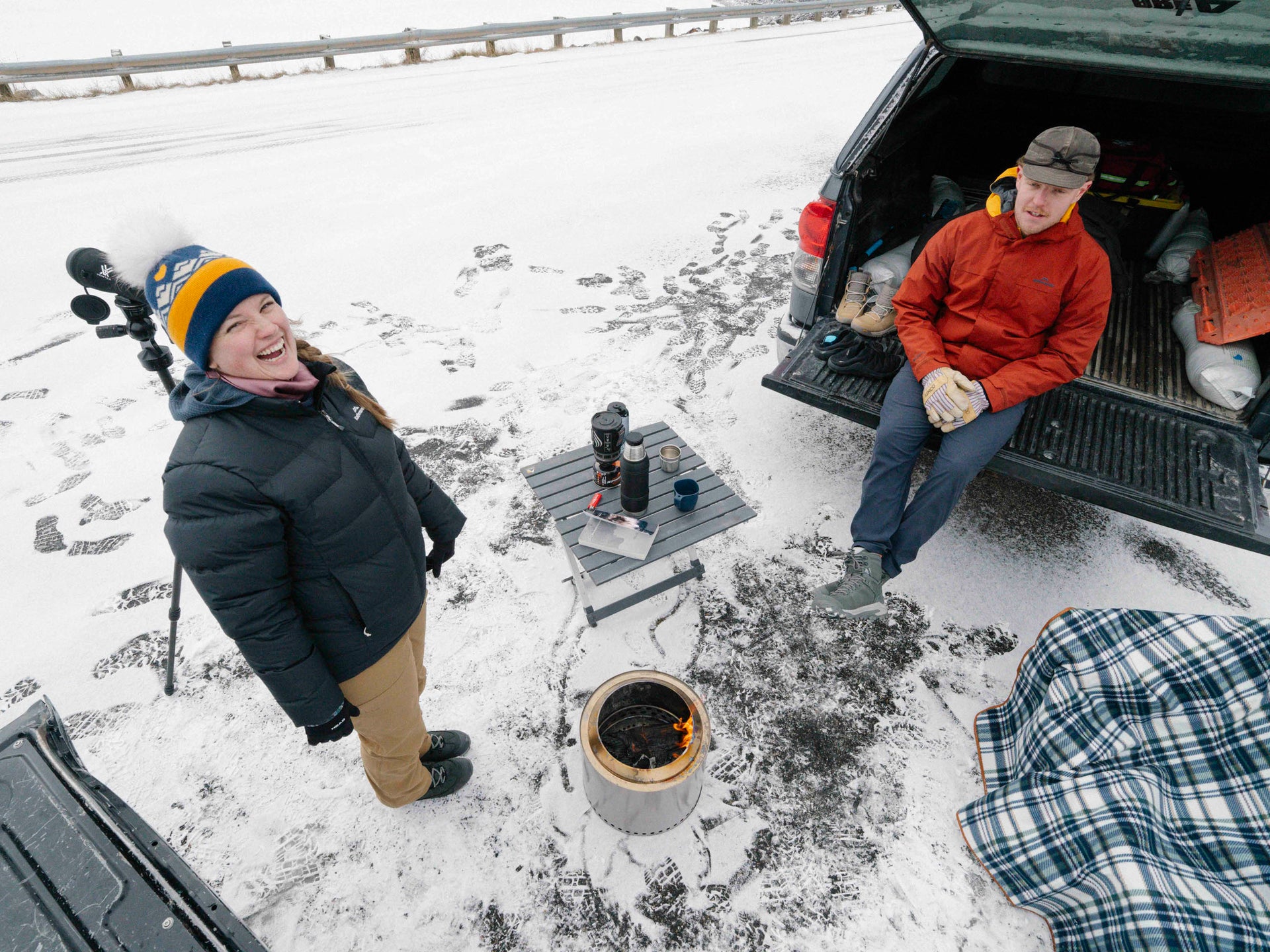 Two people in a snowy setting with a portable stove and backpacks.