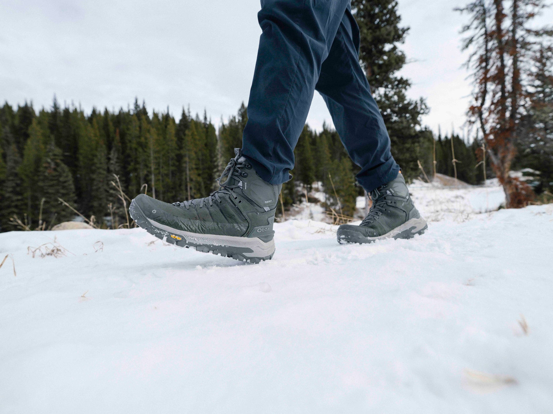 Person wearing Charcoal gray Oboz Bangtail winter boots walking on a snowy path with trees in the background