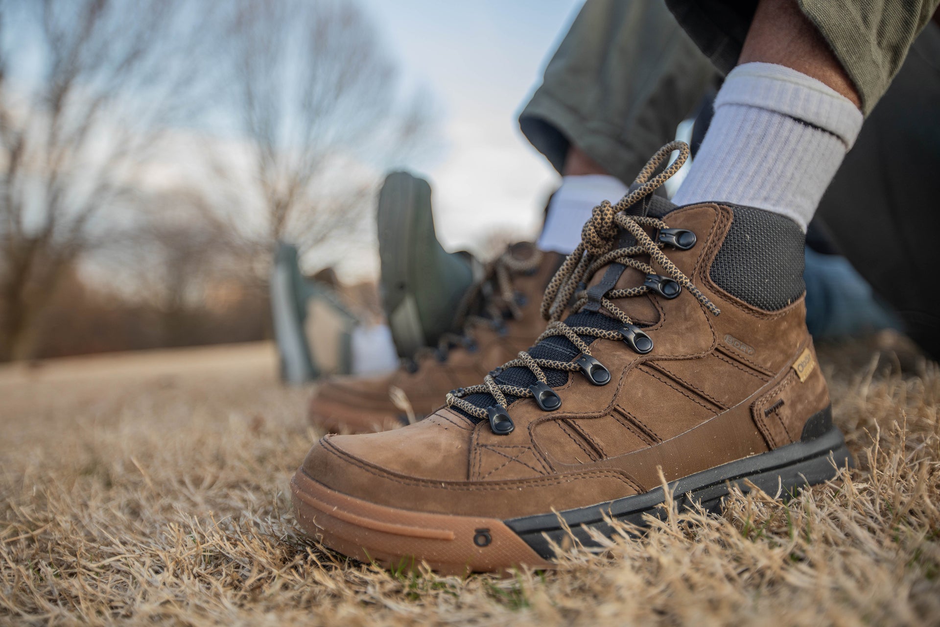 Brown Oboz Burke Mid boots on a grassy ground with blurred background