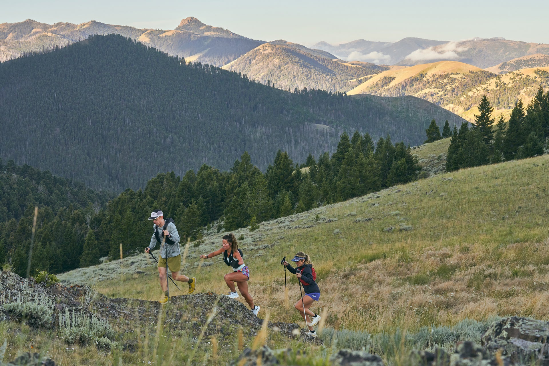 Three people hiking on a trail with mountains in the background wearing Oboz Katabatic Wind trail running shoes