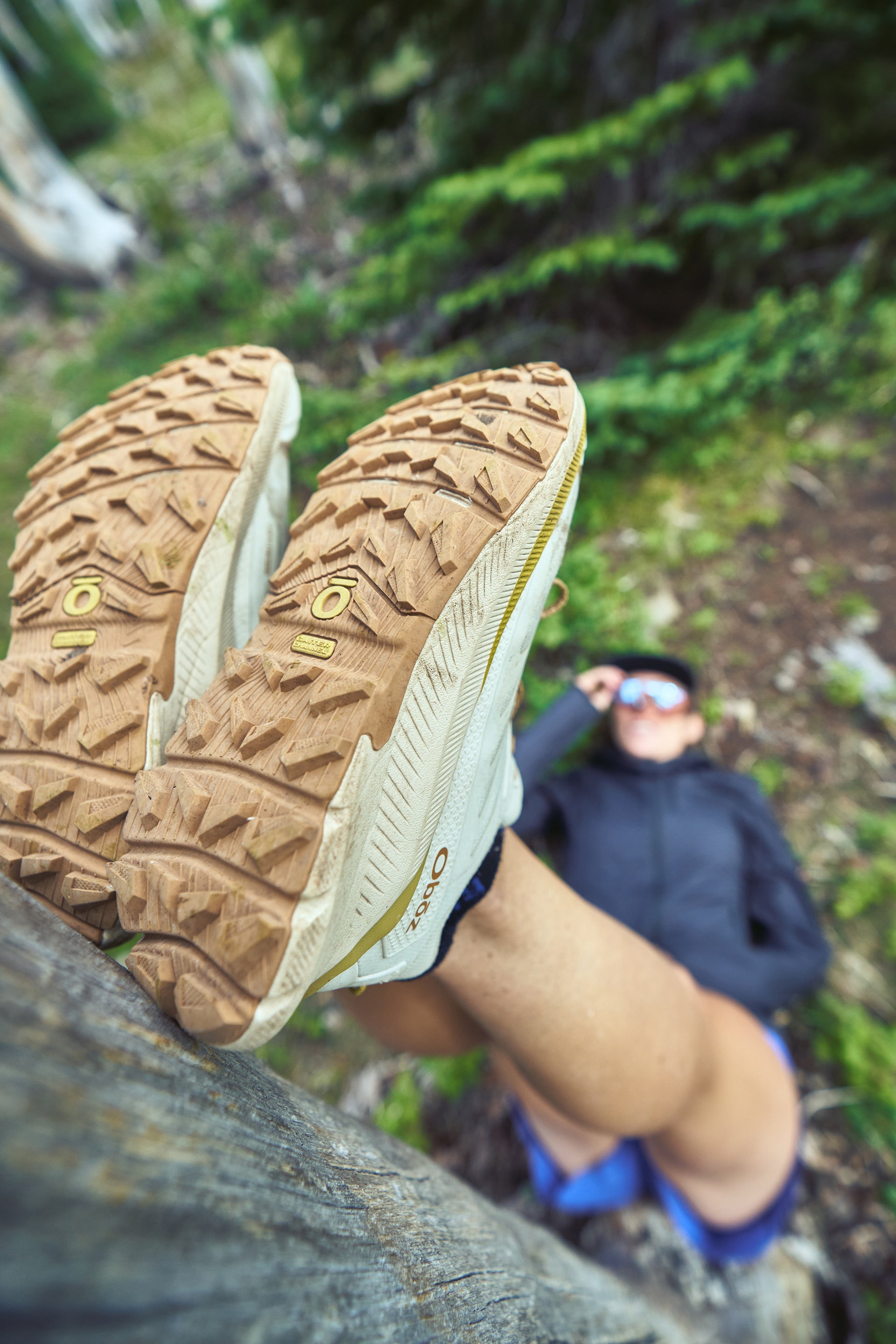 Close-up of Oboz Katabatic Wind trail running shoes with a person in the background on a forest trail