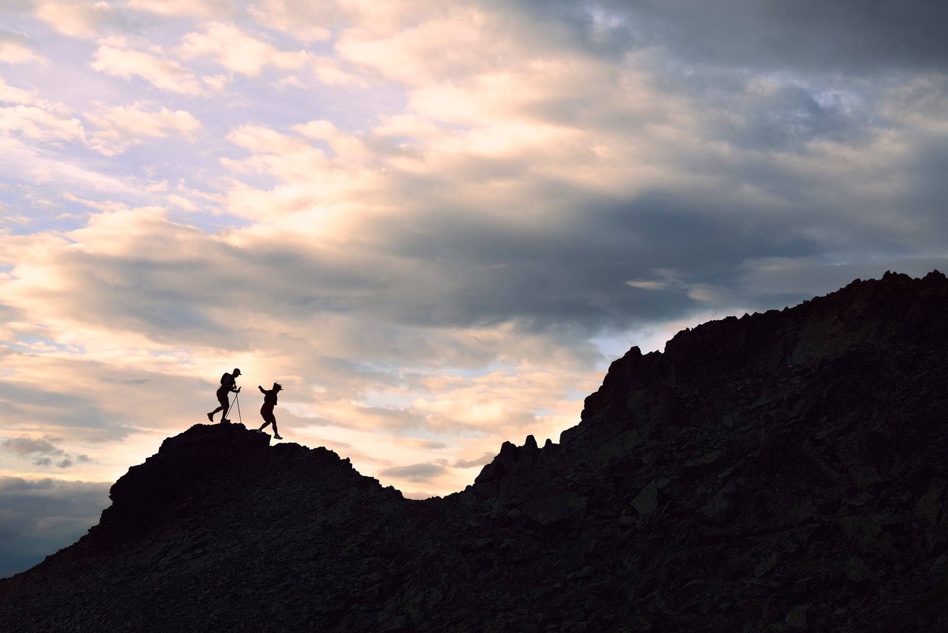 Two people standing on a rocky outcrop against a dramatic sky with clouds wearing Oboz Katabatic Wind trail running shoes