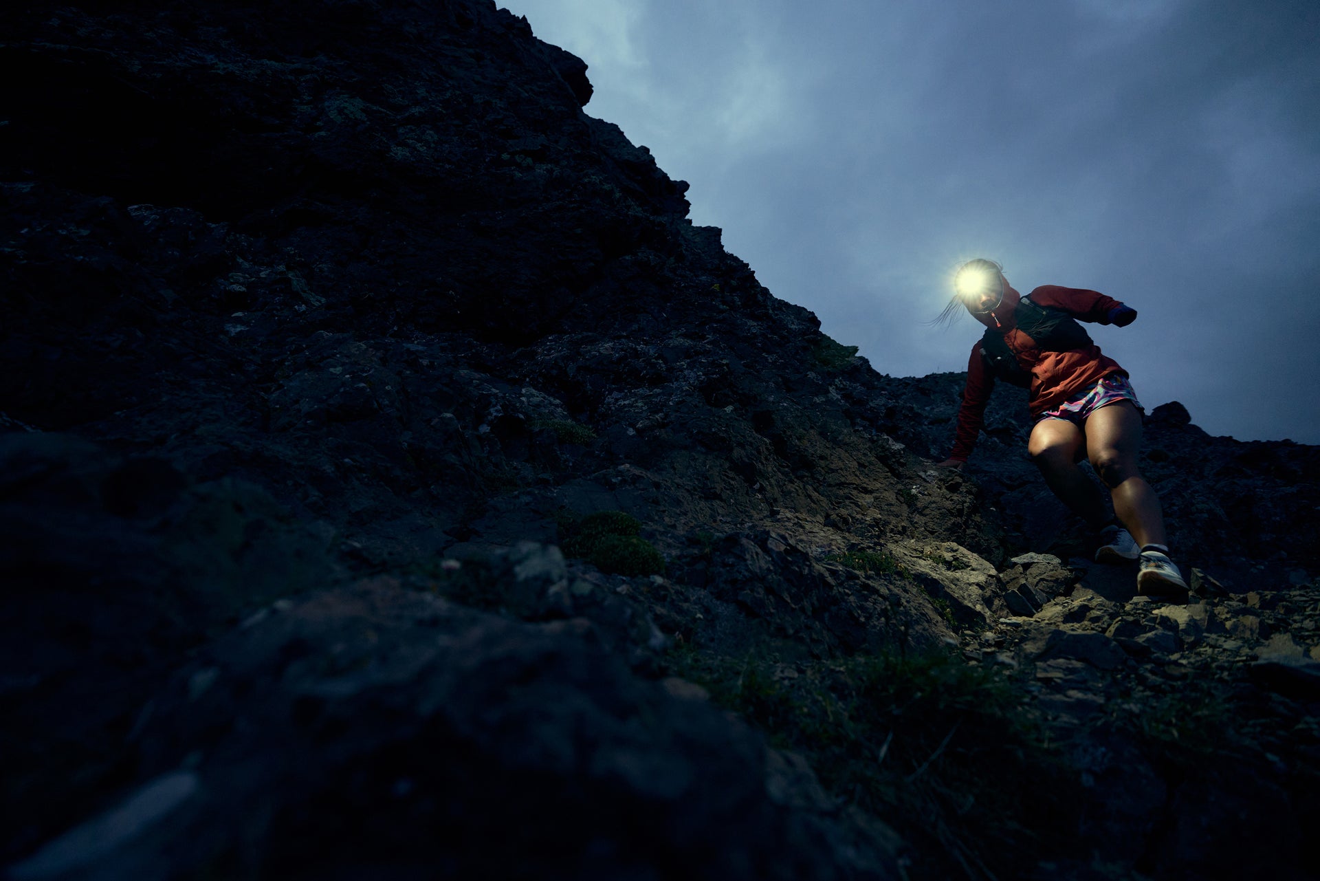 Person hiking a rocky mountain at night with a headlamp.