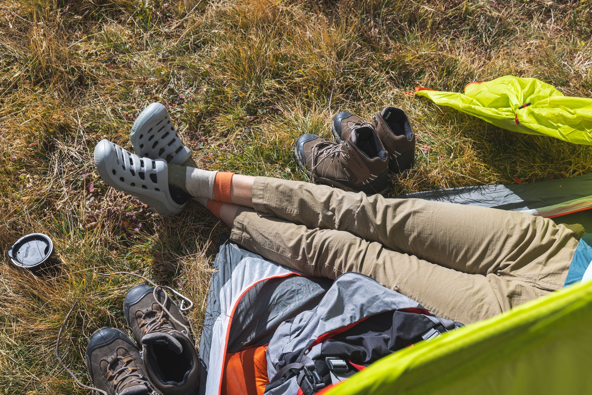 Person lying on a grassy field with camping gear around wearing Oboz Whakata Coast sandals.