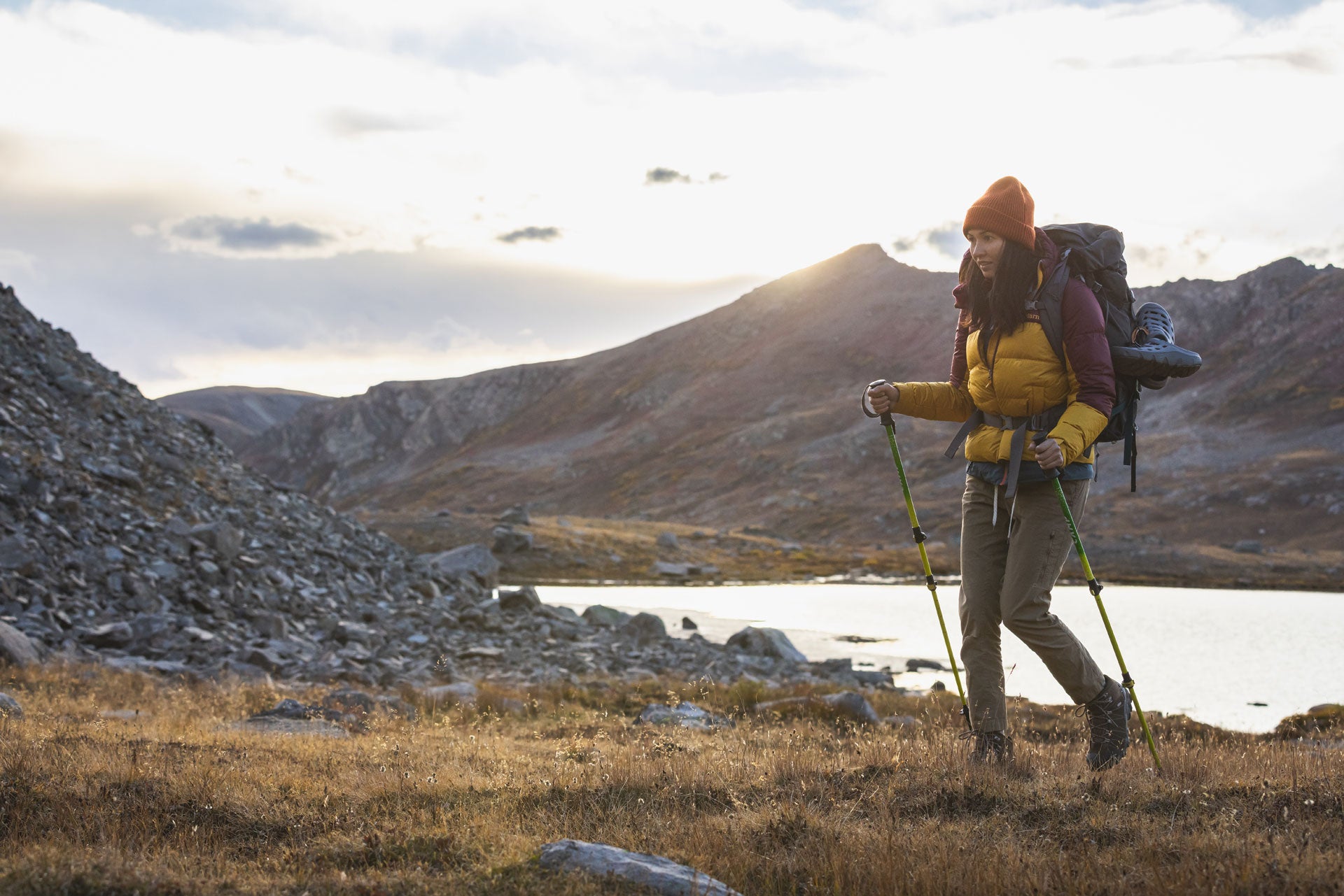 Person hiking with a backpack and poles in a mountainous landscape with a lake.