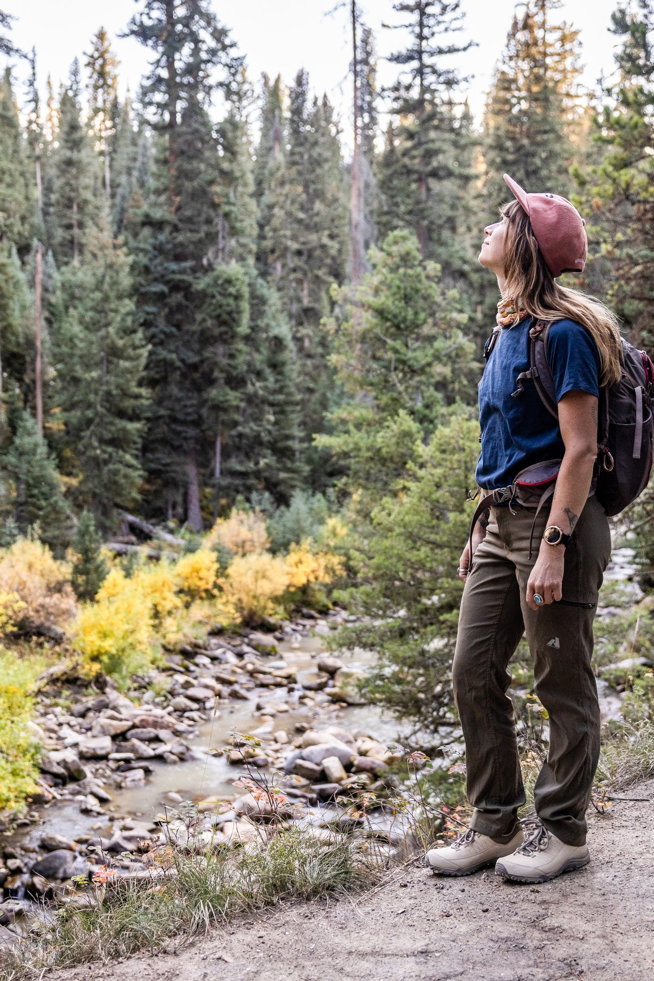 Person hiking on a trail through a forest with backpack and hat