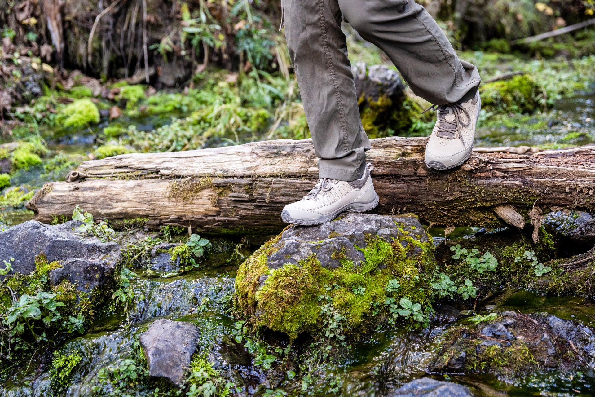 Person walking on a log over a stream in a forest while wearing Oboz Ousel hiking shoes.