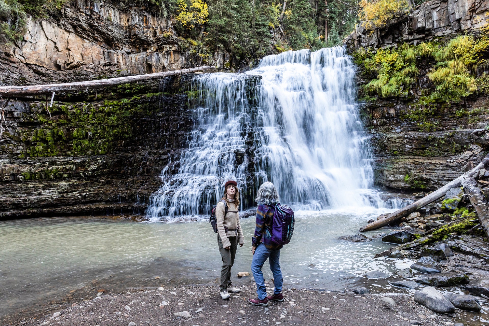 Two people standing in front of a waterfall while on a hike