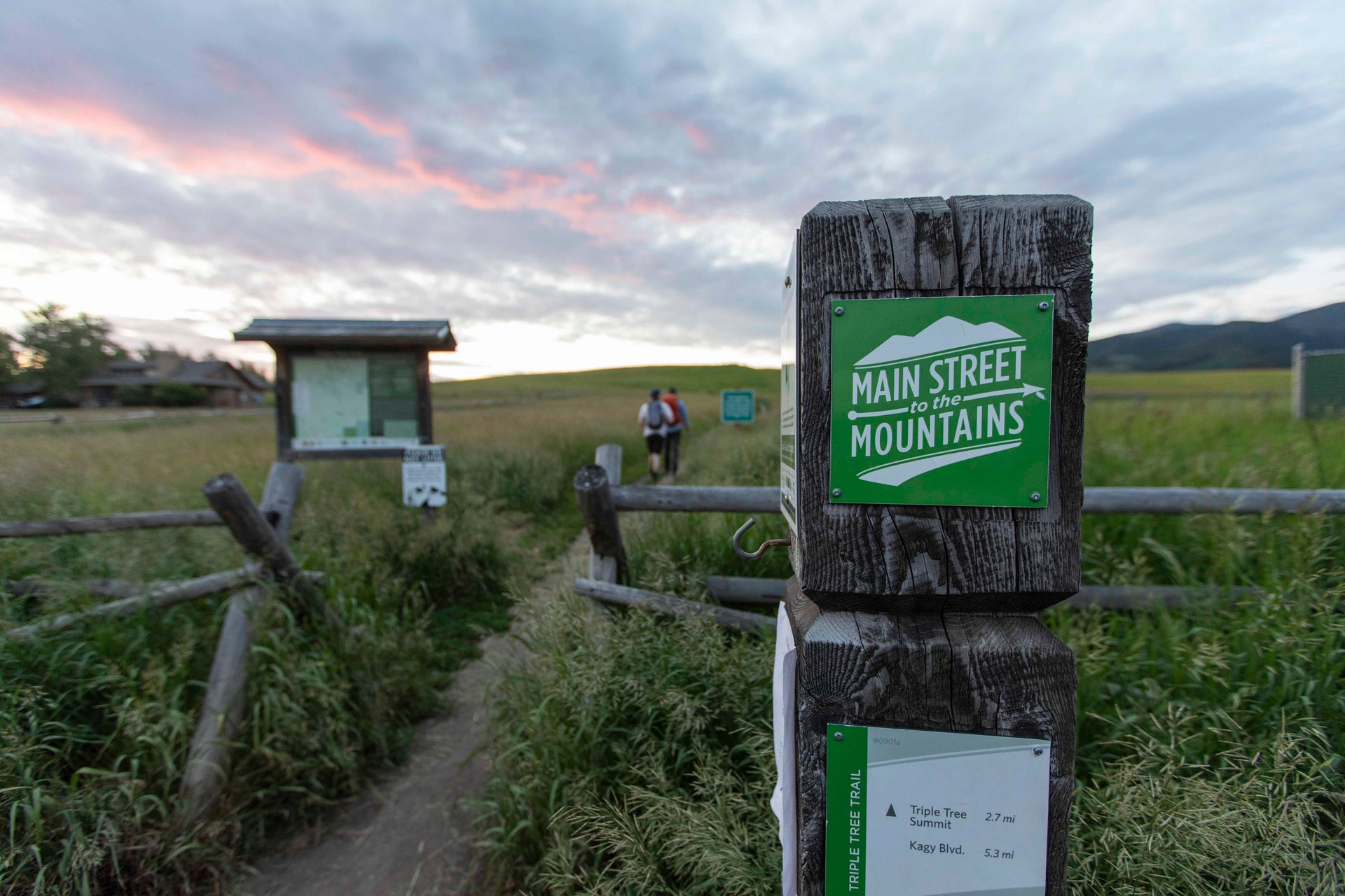 Trailhead signpost with Bozeman's, 'Main Street Mountains' on a grassy field at dusk.