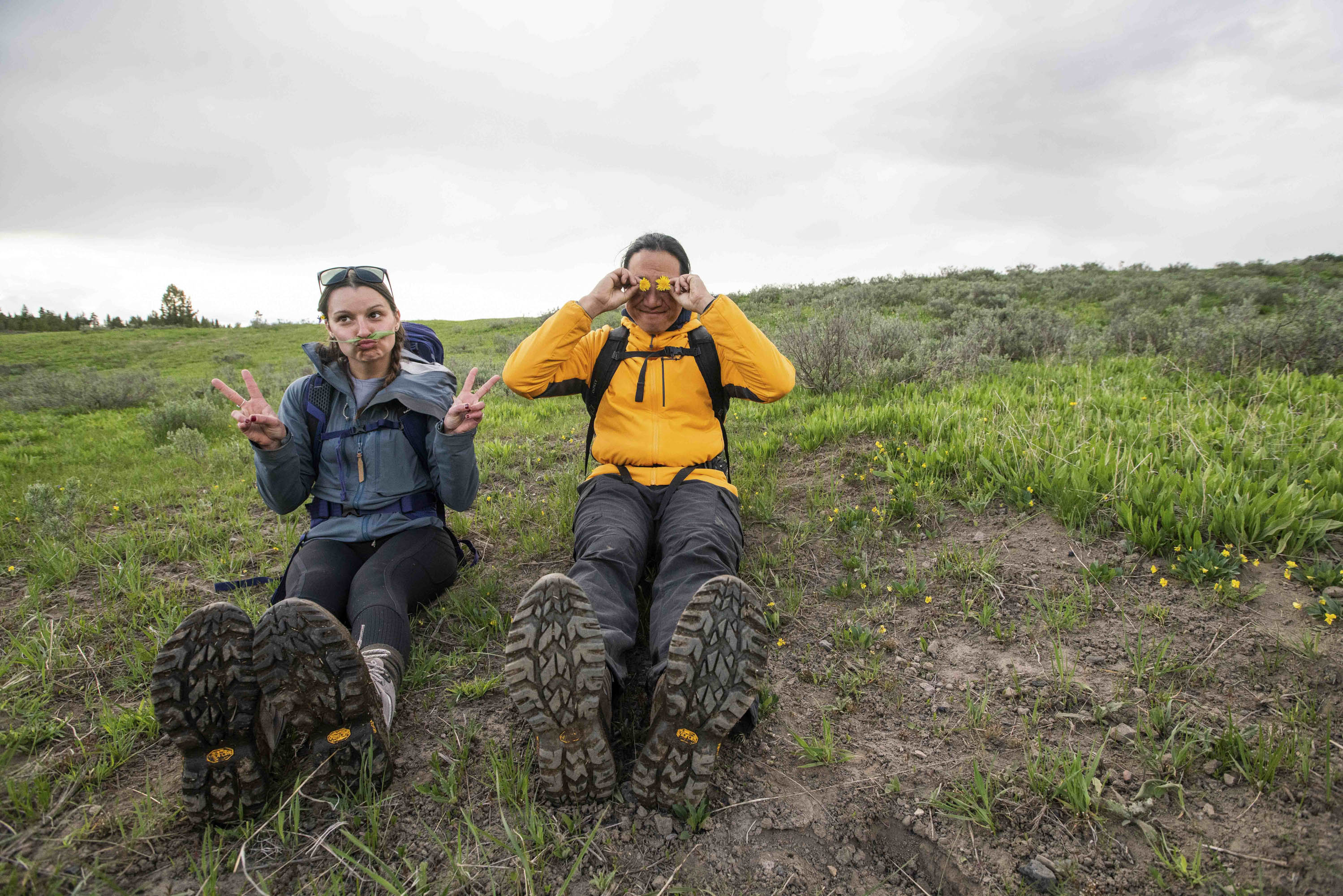 Two people sitting on a grassy hillside wearing Oboz Sawtooth Ascent hiking boots.