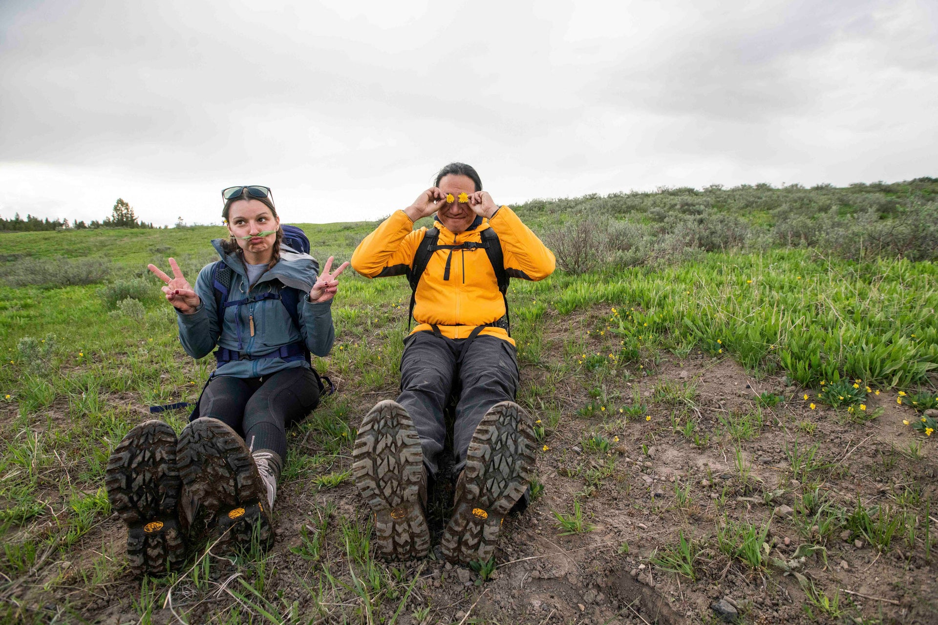 Two people sitting on a grassy hillside wearing Oboz Sawtooth Ascent hiking boots.