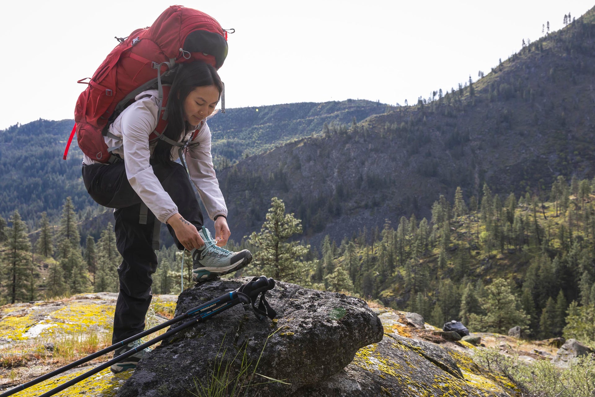 Person with a red backpack lacing up a pair of Oboz Bridger Ridge hiking boots