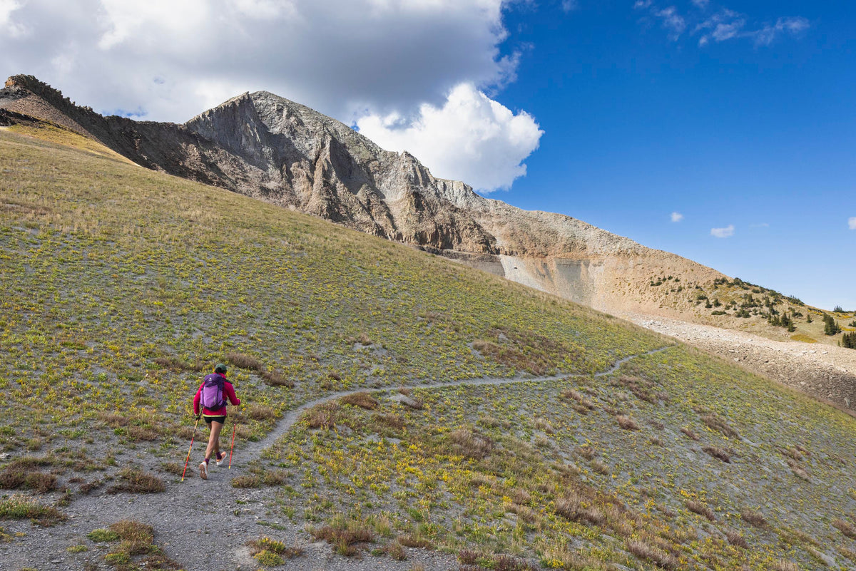 Person hiking on a mountain trail with a scenic view of mountains and blue sky.