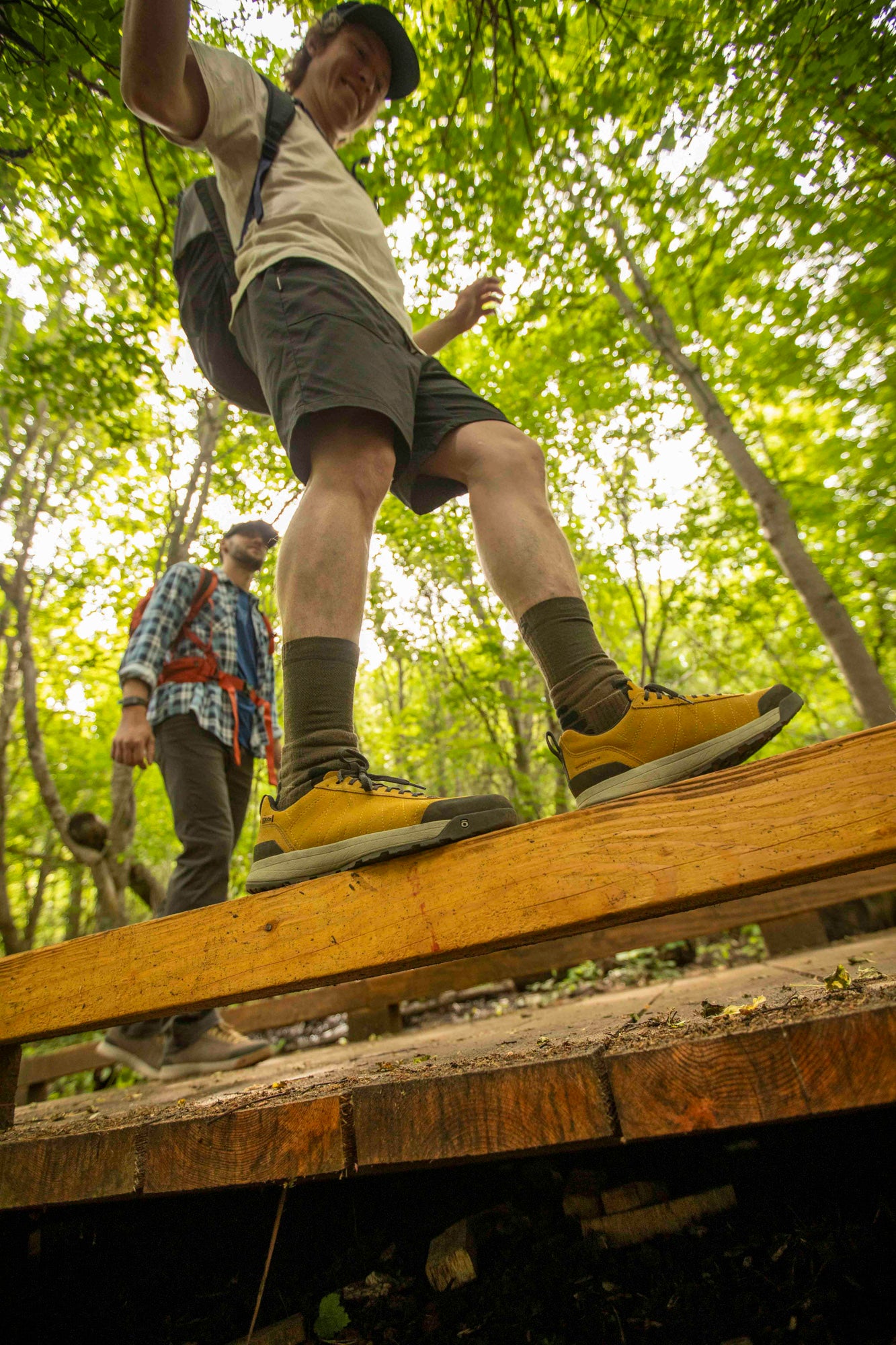 Person walking on a wooden plank in a forest setting, wearing Oboz Bozeman II hiking shoes