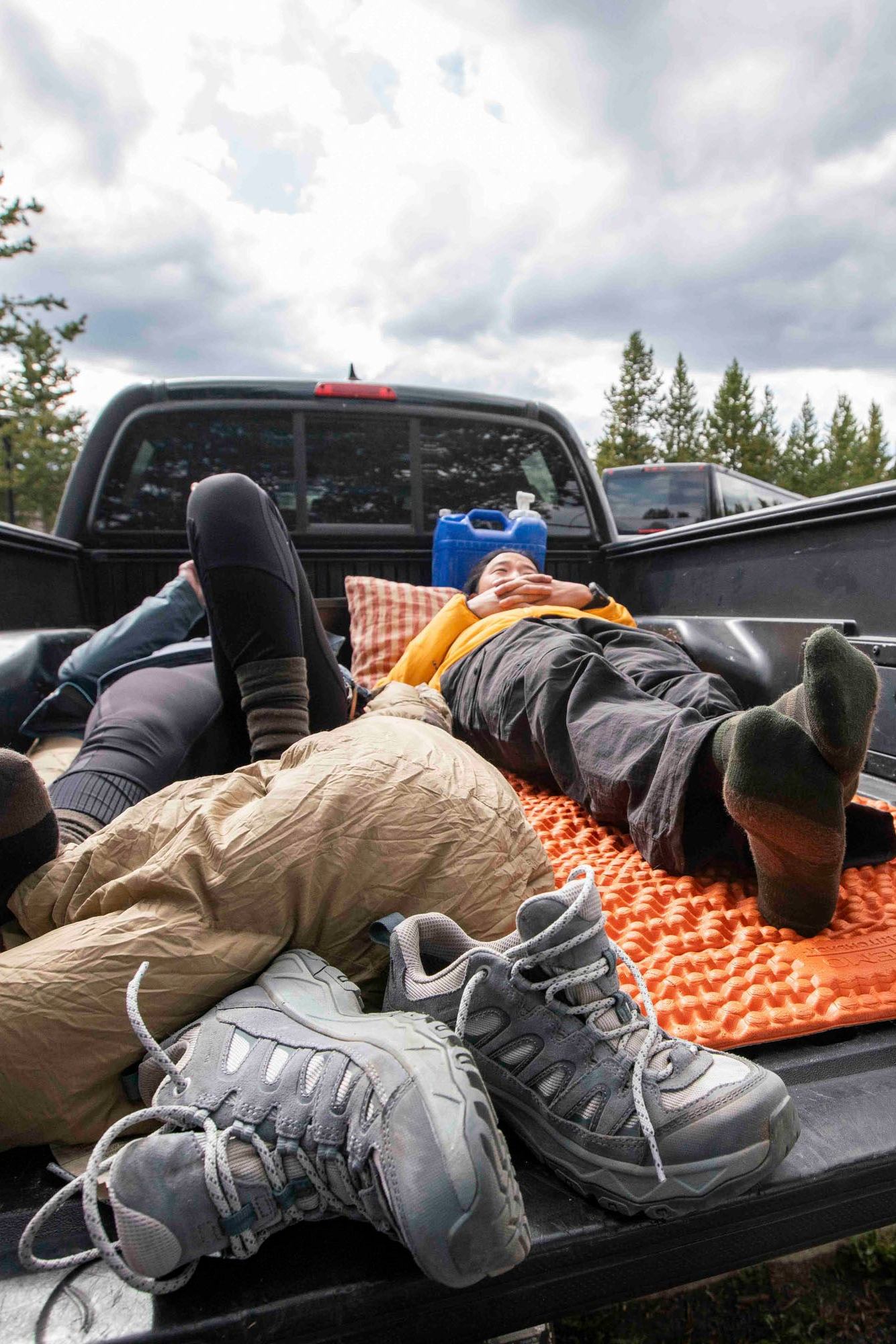 Two hikers lying on an orange sleeping pad in the back of a pickup truck after a long hike.