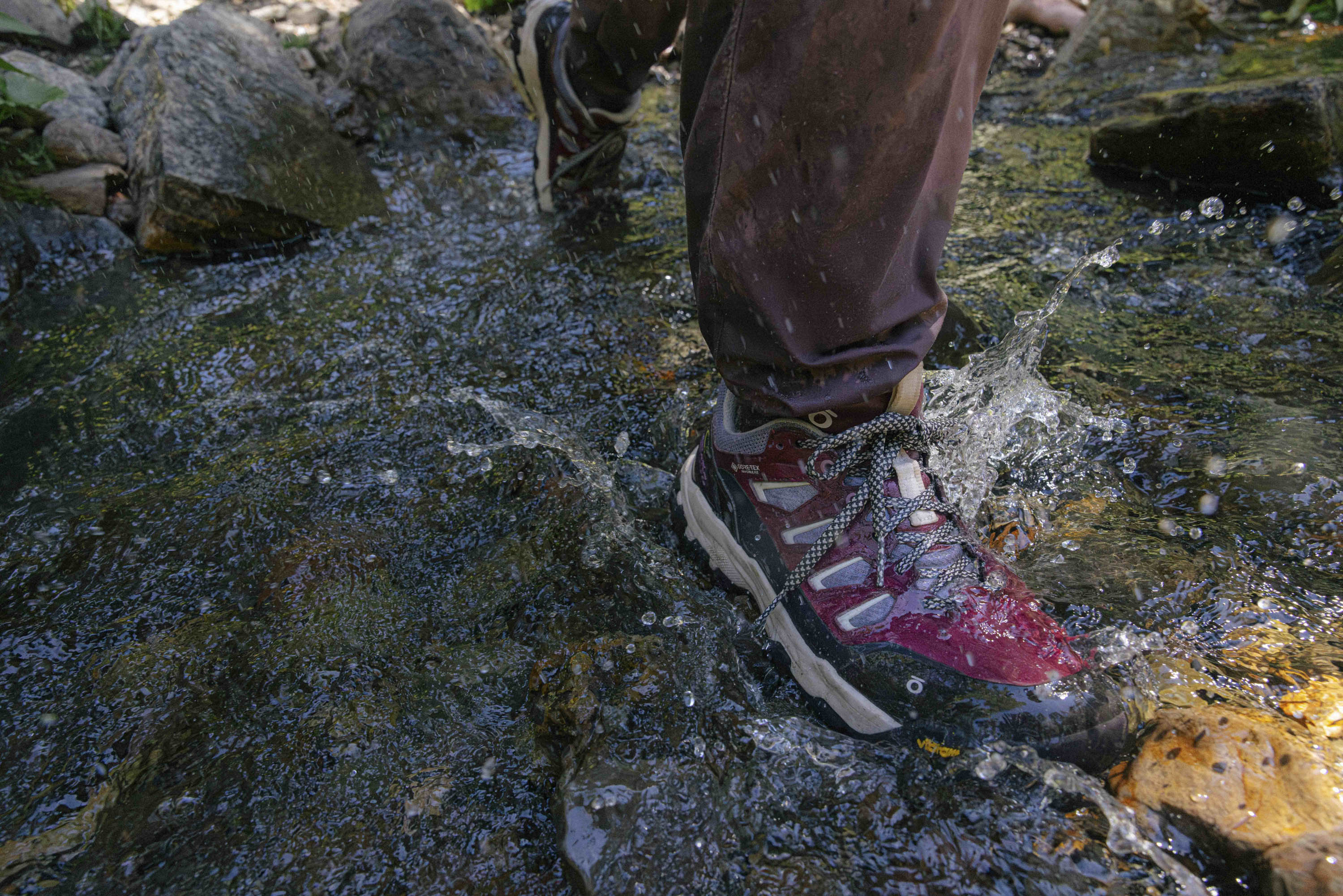 Person wearing Oboz Sawtooth X PRO hiking boots stepping into a stream with water splashing around.