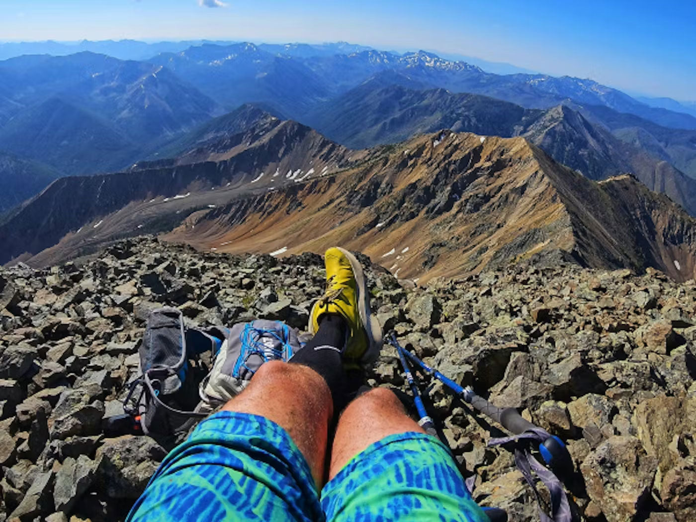 Person sitting on a mountain peak with a breathtaking view of the surrounding mountains.