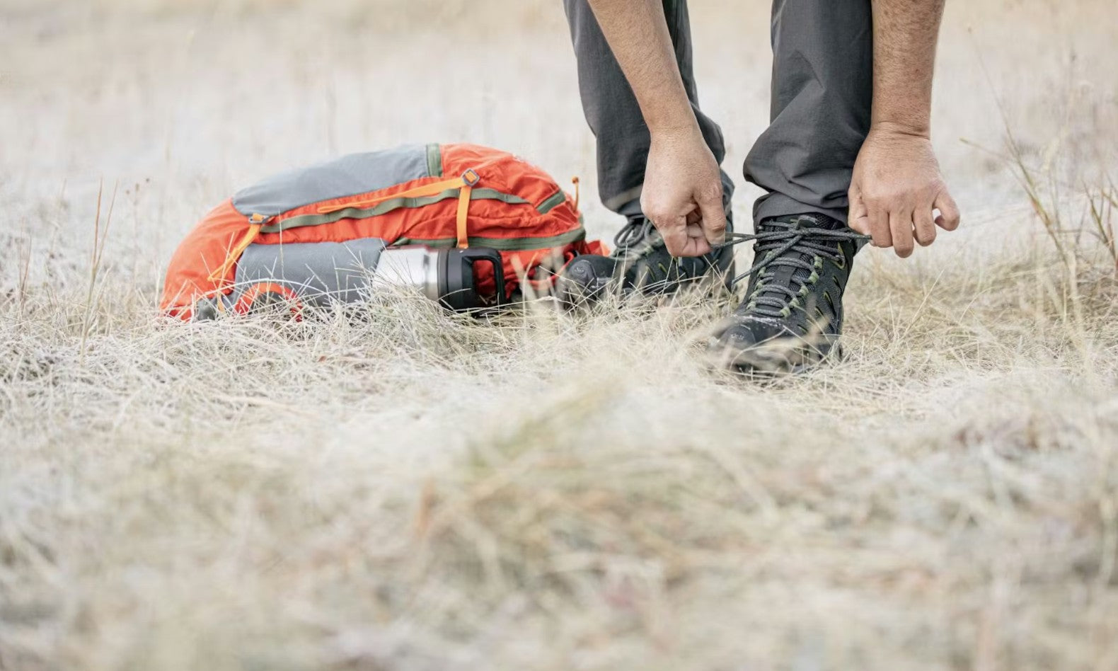 Person adjusting the Oboz Sawtooth II Mid hiking boots in gray with a backpack in a grassy field